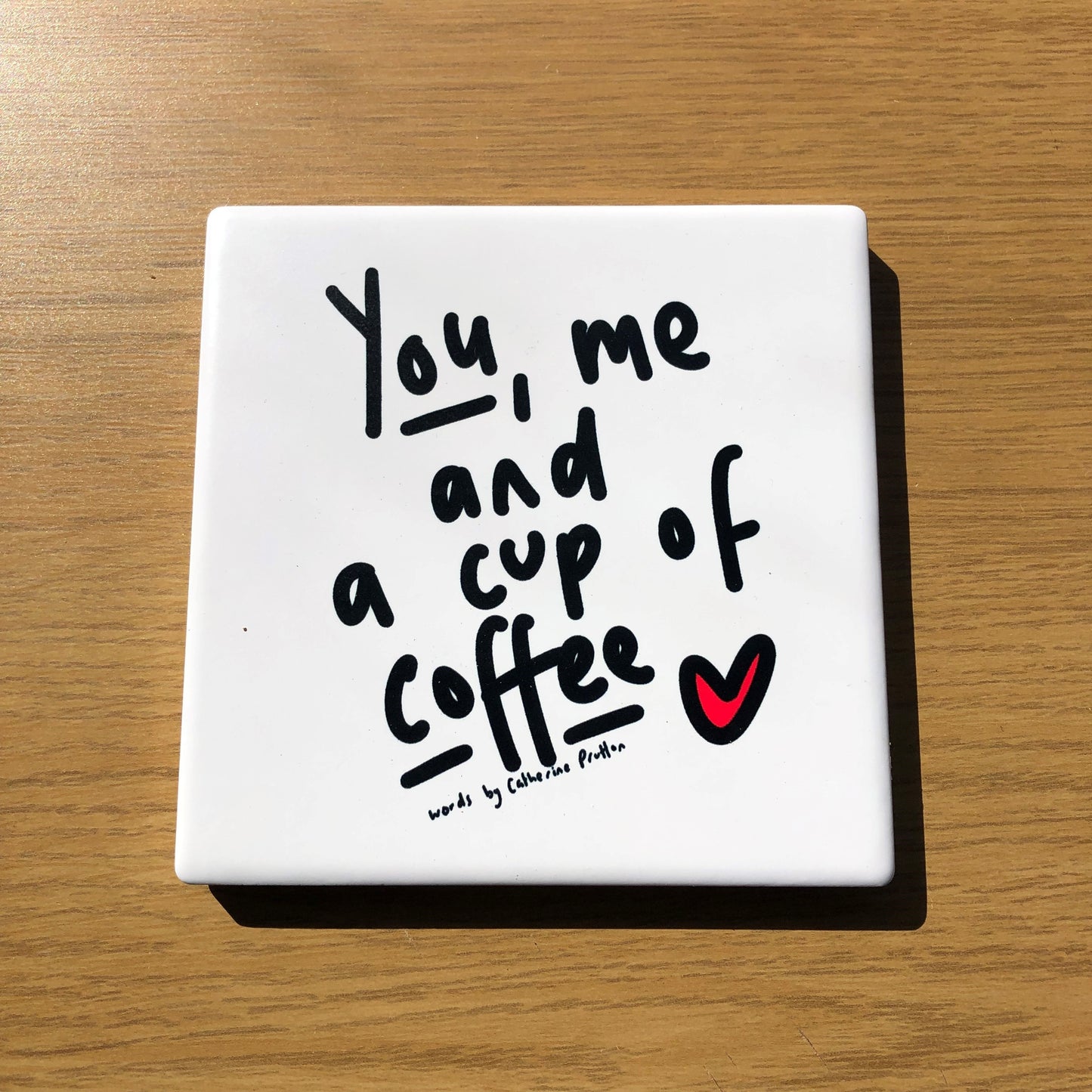 Ceramic coaster featuring the phrase “You, Me and a Cup of Tea” in handwritten style, designed by Catherine Prutton, with cork backing.