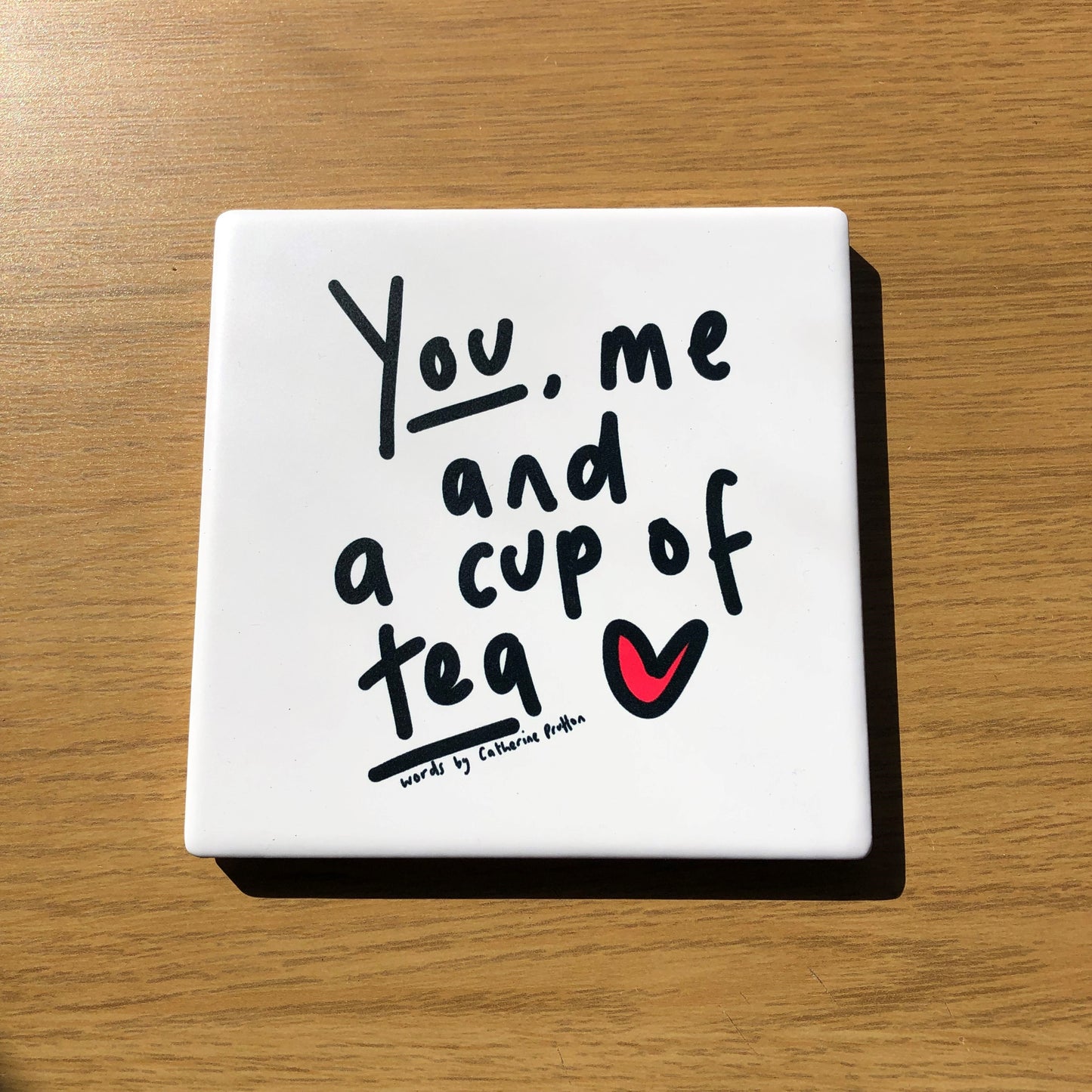 Ceramic coaster with the words “You, Me and a Cup of Coffee” in handwritten script, designed by Catherine Prutton, with cork backing.